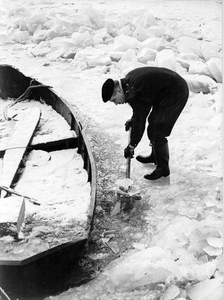 361199 Afbeelding van een man bij een vastgevroren bootje tijdens de winter van 1963.
